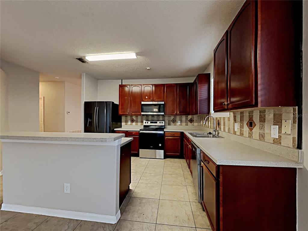 A kitchen features dark wood cabinets, black appliances, light countertops, and a tiled backsplash — 716 KNOLLWOOD DRIVE, DAVENPORT, FL
