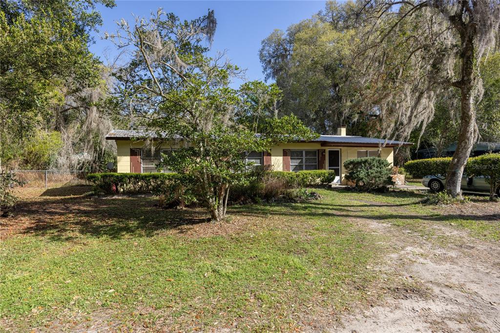 A single-story yellow house with a metal roof sits on a grassy, tree-filled lot — 1610 SE 25TH AVENUE, GAINESVILLE, FL