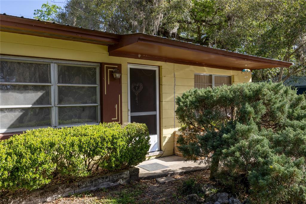 A single-story yellow house with a metal roof sits behind a landscaped front yard — 1610 SE 25TH AVENUE, GAINESVILLE, FL