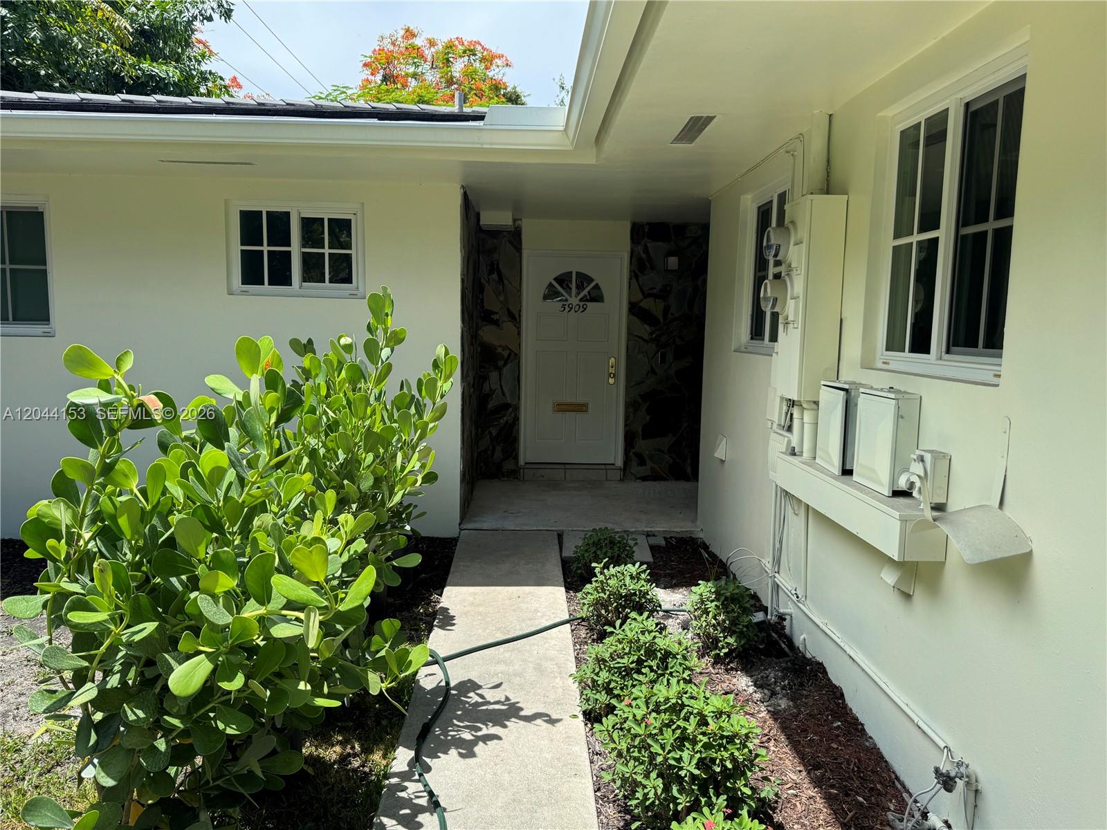 A concrete walkway leads to a white front door recessed into a stone-accented entryway — 5907 Turin St # 5909, Coral Gables FL 33146, CORAL GABLES, FL