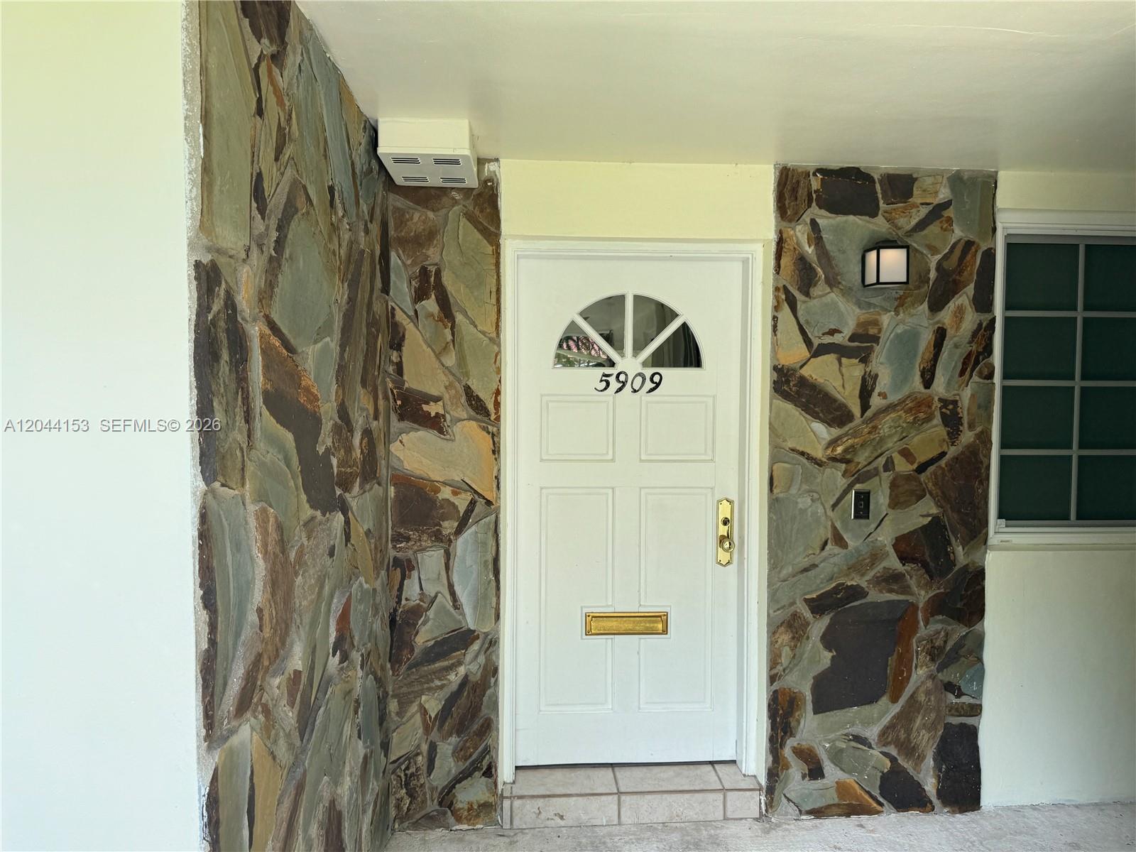 A white front door with a gold mail slot is flanked by natural stone walls — 5907 Turin St # 5909, Coral Gables FL 33146, CORAL GABLES, FL