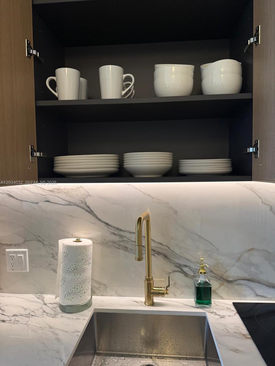A kitchen features a marble backsplash, gold faucet, and open cabinets with white dishware — 2700 NW 2ND AVE # 209, Miami FL 33127, MIAMI, FL