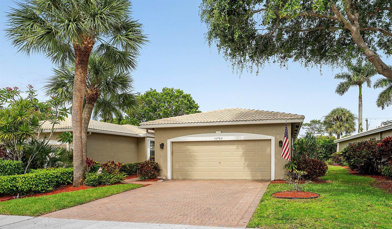 A single-story house with a beige garage, a brick driveway, and palm trees in front — 10760 Royal Caribbean Circle, Boynton Beach FL 33437, BOYNTON BEACH, FL