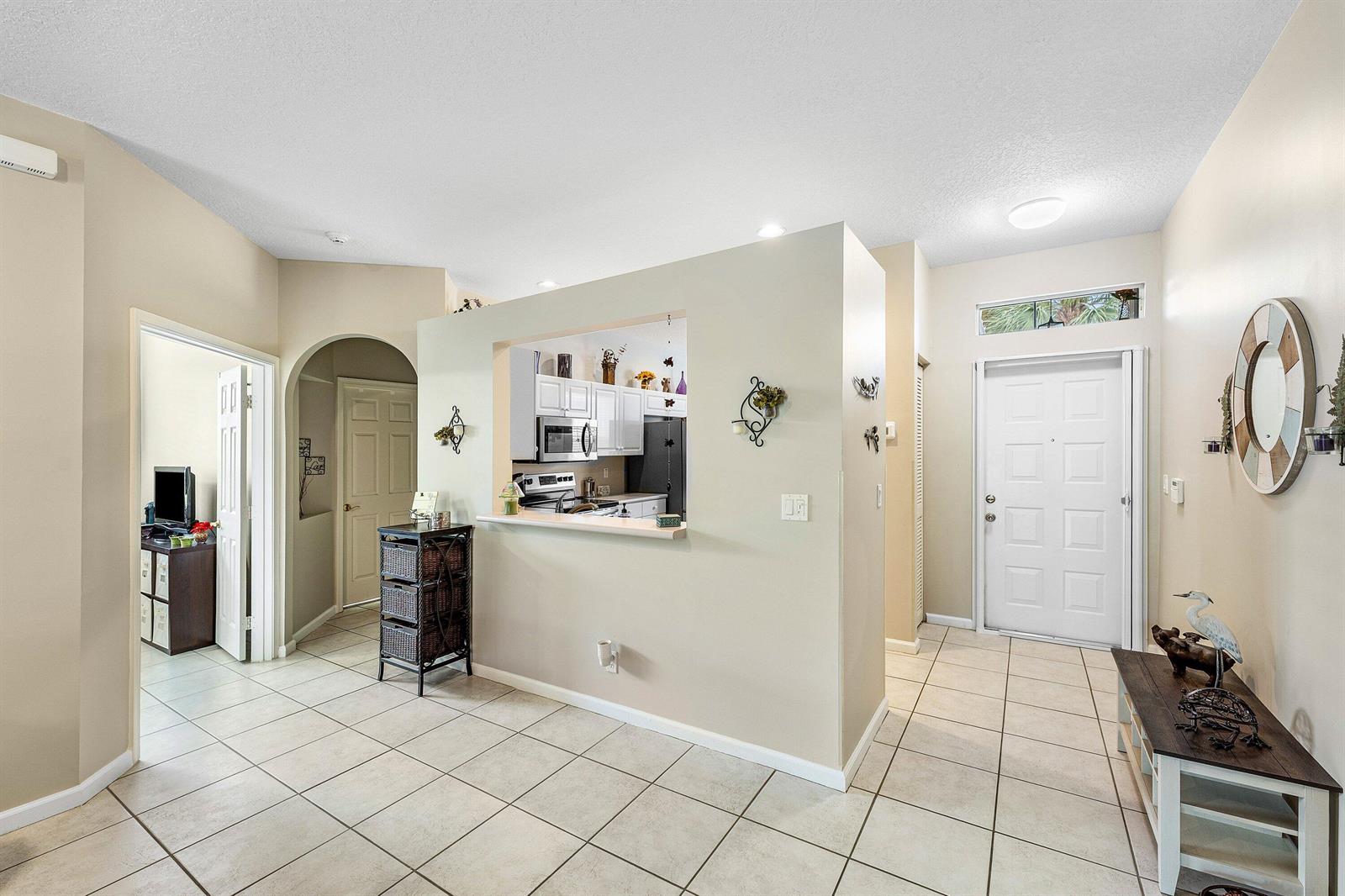 An entryway with tile flooring leads to a kitchen pass-through window and a front door — 10760 Royal Caribbean Circle, Boynton Beach FL 33437, BOYNTON BEACH, FL