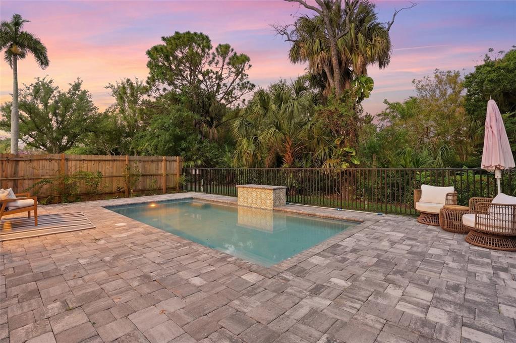 A rectangular swimming pool with a stone water feature sits on a paved patio — 1473 BARCELONA AVENUE, FORT MYERS, FL