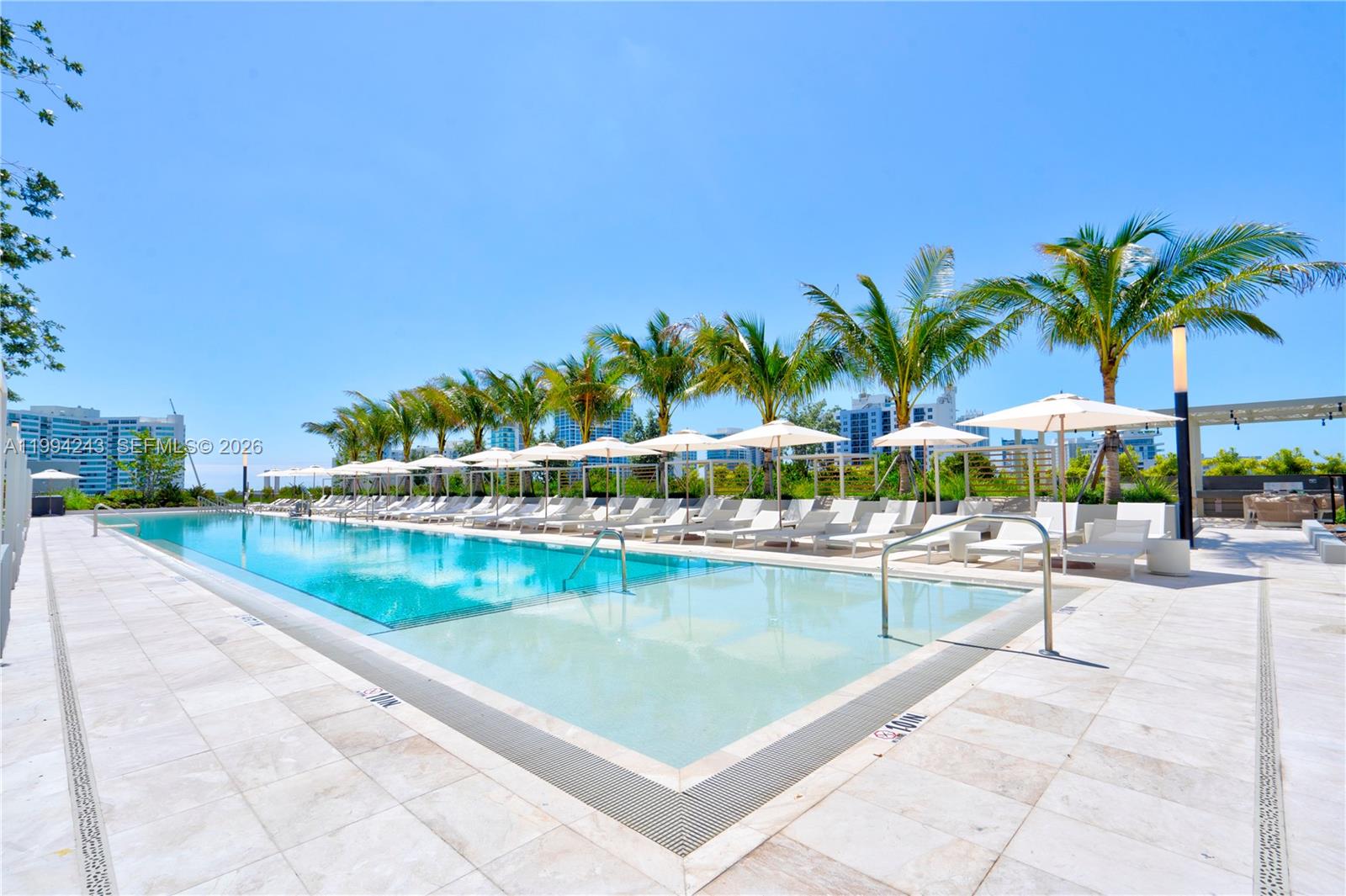 A long outdoor swimming pool is surrounded by lounge chairs, umbrellas, and palm trees — 580 72nd St # 1708, Miami Beach FL 33141, MIAMI BEACH, FL