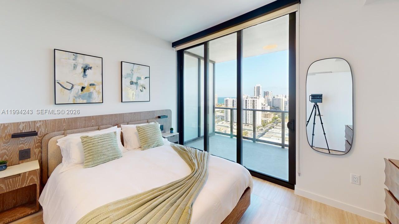 A bedroom features a bed with green pillows, wood accents, and a balcony with city views — 580 72nd St # 1708, Miami Beach FL 33141, MIAMI BEACH, FL