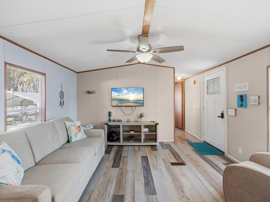 A living room features light wood-look flooring, a beige sofa, a television, and a ceiling fan — 6419 W RICHARD DRIVE, WEEKI WACHEE, FL