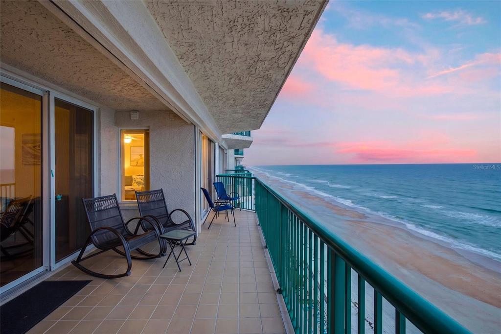 A balcony with tile flooring and rocking chairs overlooks the ocean at sunset — 3315 S ATLANTIC AVENUE UNIT 1406, DAYTONA BEACH SHORES, FL