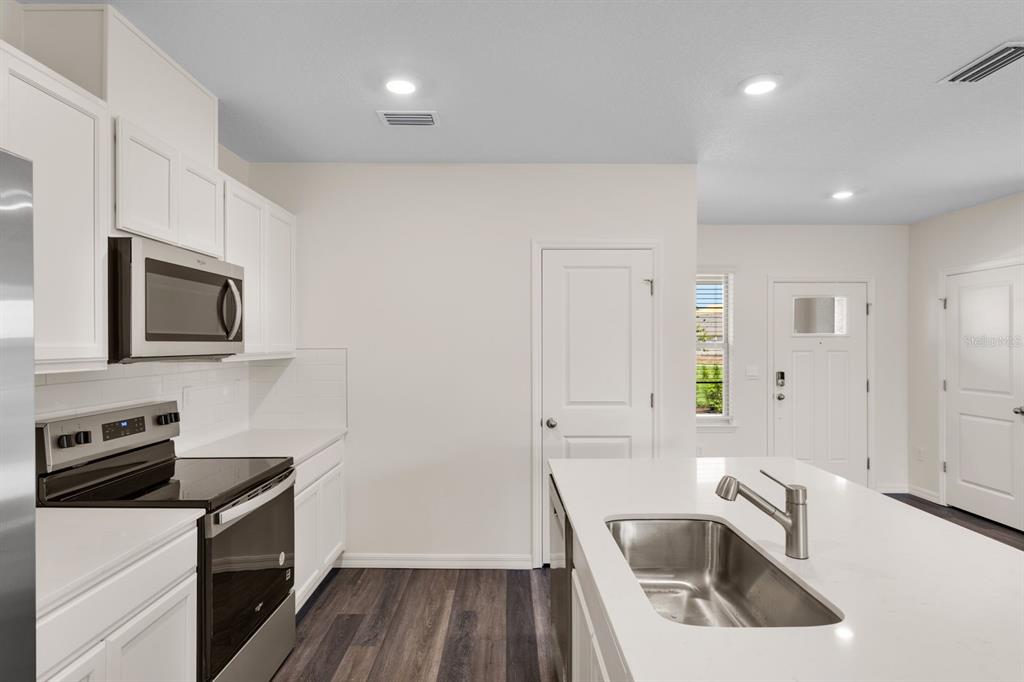 A modern kitchen features white cabinets, stainless steel appliances, and a large central island — 16558 BARBOURS CREEK WAY, WINTER GARDEN, FL