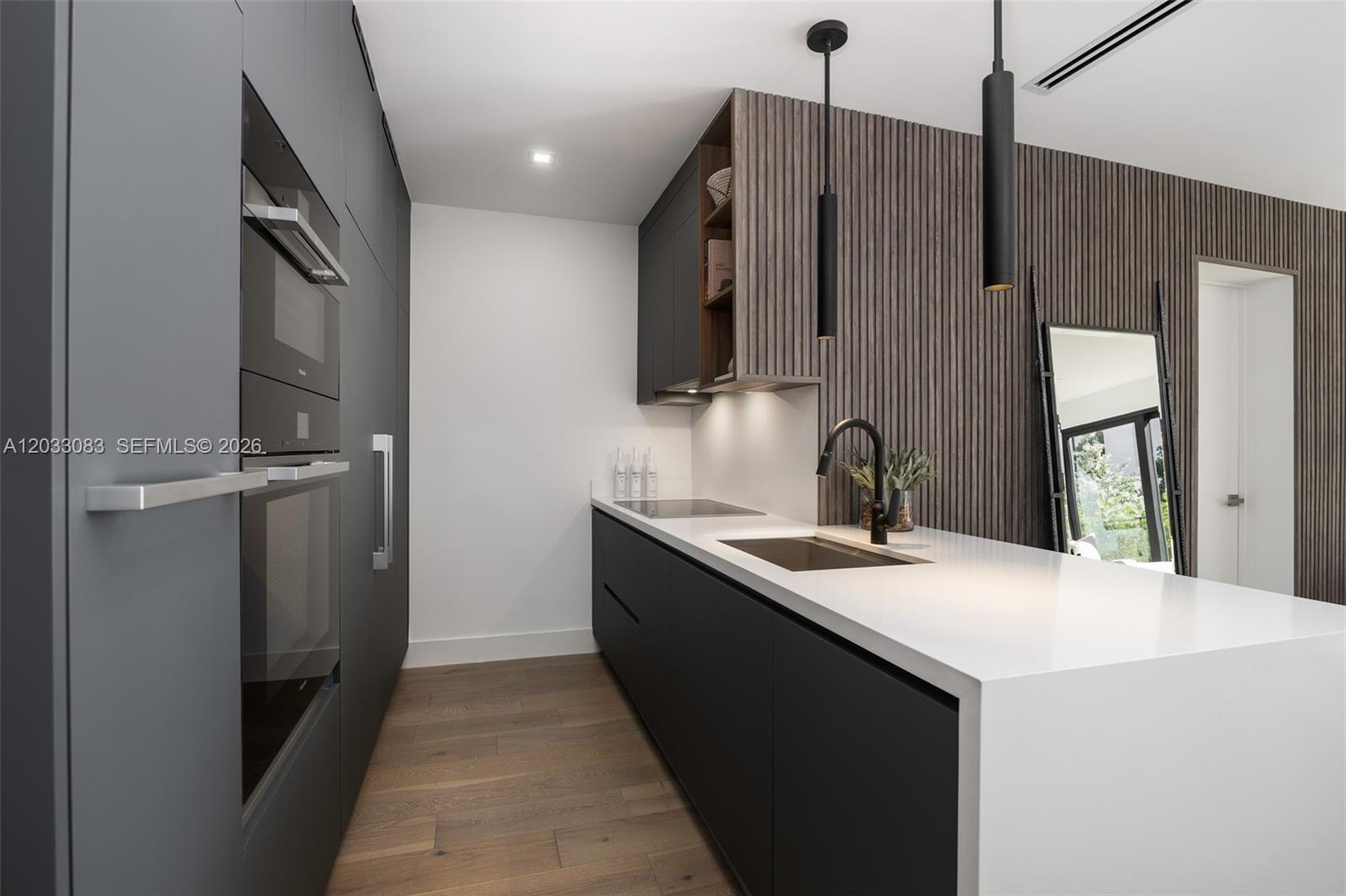A modern kitchen features dark cabinetry, white countertops, wood-slat wall paneling, and two pendant lights — 202 Sunrise Dr # 202B, Key Biscayne FL 33149, KEY BISCAYNE, FL