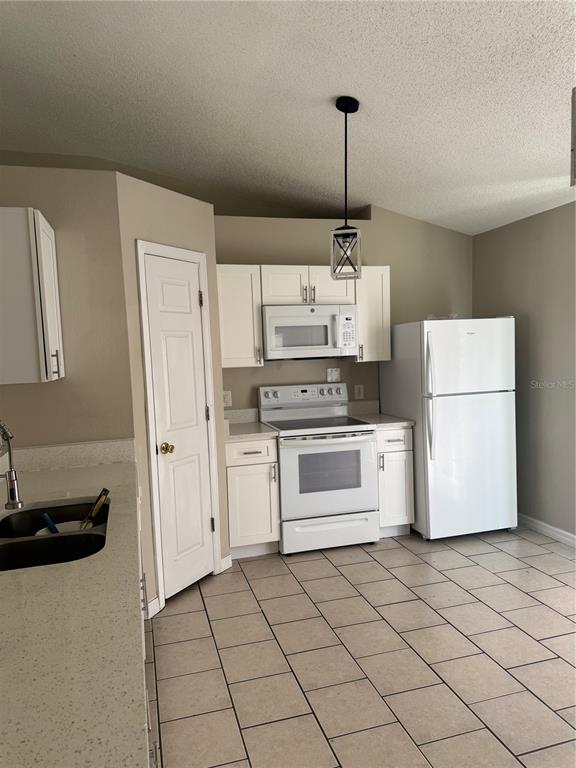 A kitchen features white cabinets, white appliances, a tiled floor, and a single pendant light — 510 EAGLE COURT, POINCIANA, FL
