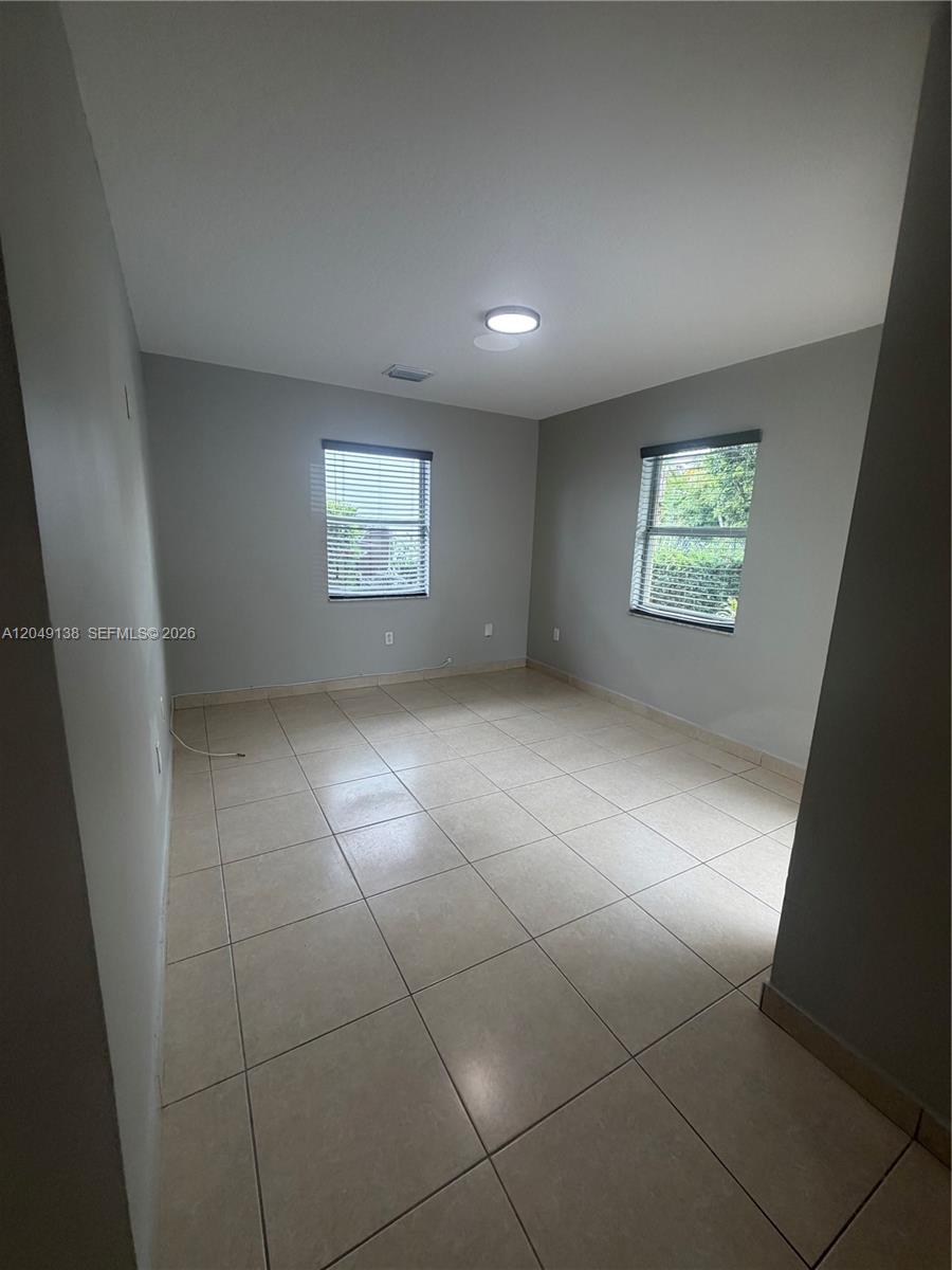 An empty room features light gray walls, beige tile flooring, and two windows with blinds — PALMETTO BAY, FL