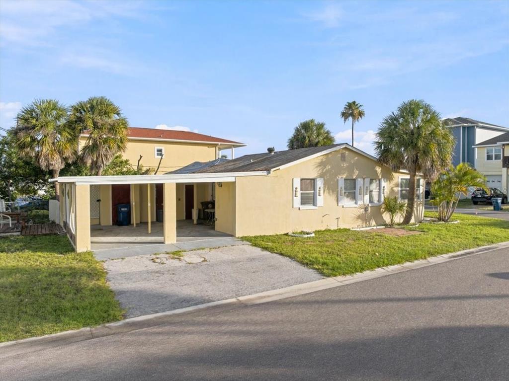 A single-story yellow house with a carport and palm trees sits along a paved street — 13104 4TH STREET E, MADEIRA BEACH, FL