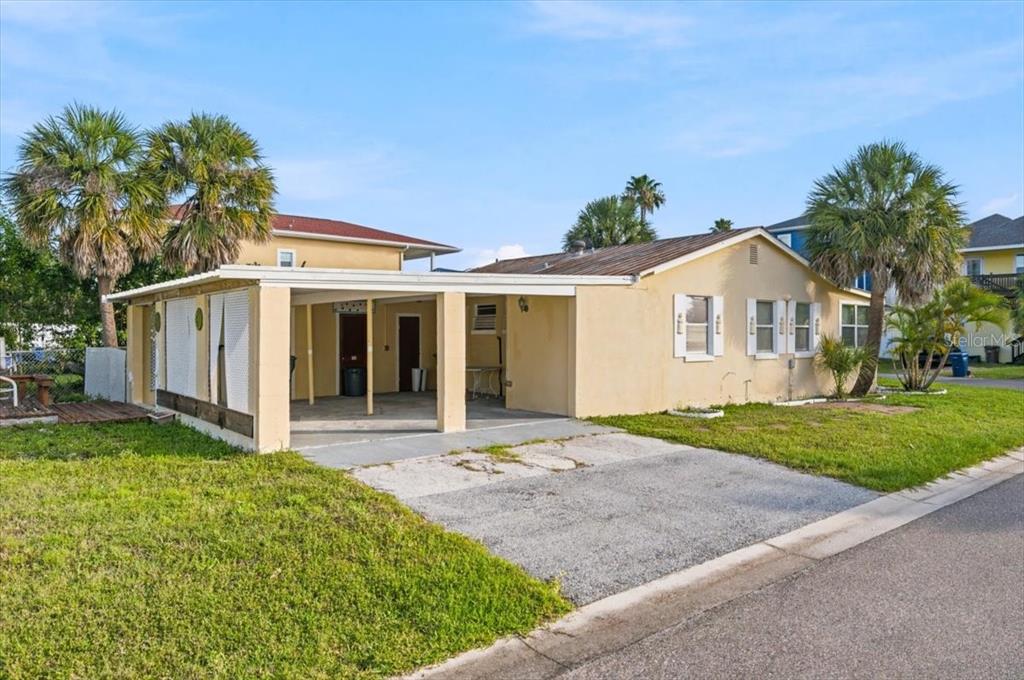 A single-story house with a carport, tan stucco exterior, and a gravel driveway — 13104 4TH STREET E, MADEIRA BEACH, FL
