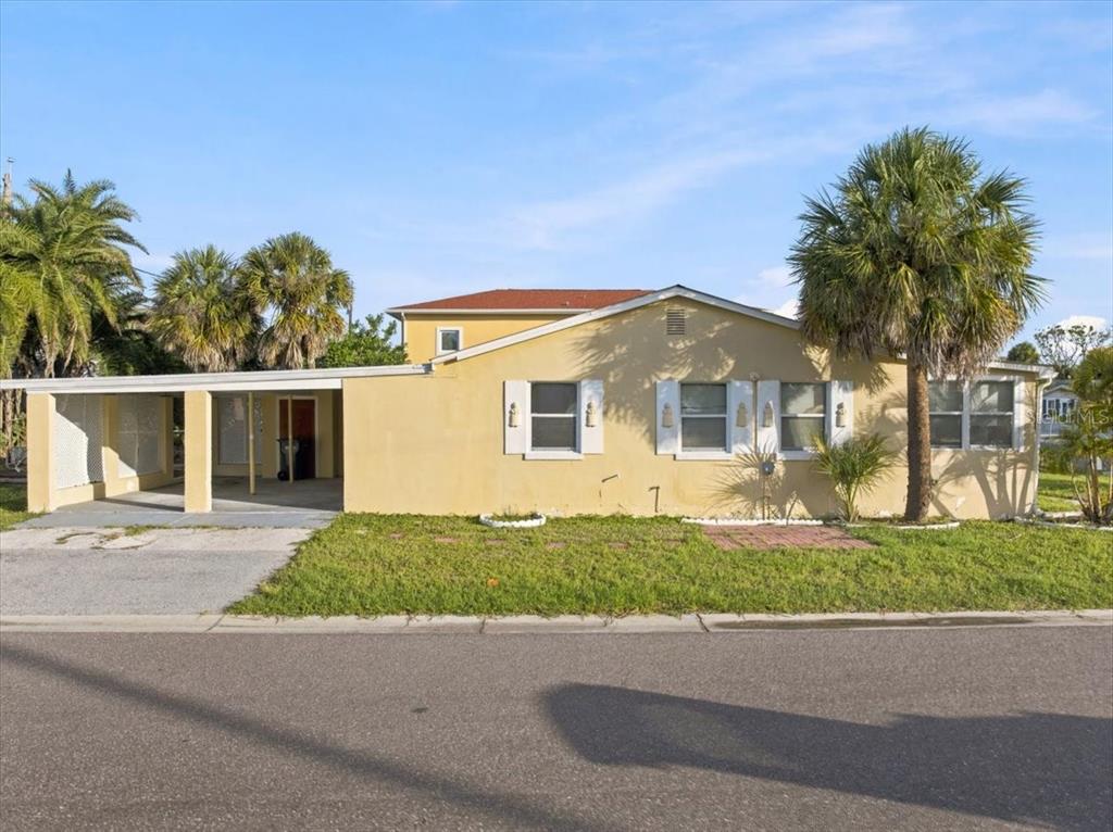 A yellow single-story house with a carport and palm trees under a blue sky — 13104 4TH STREET E, MADEIRA BEACH, FL