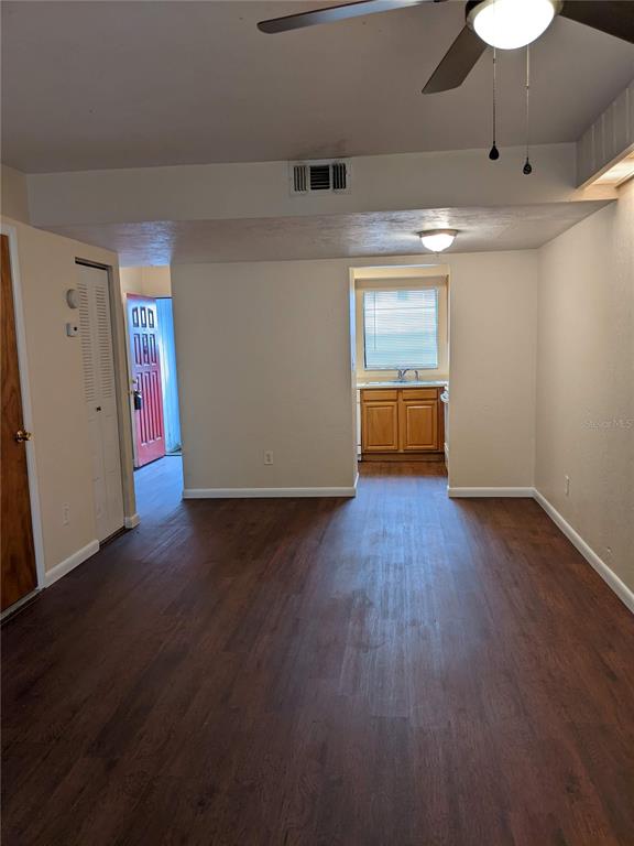 A room with dark wood-look flooring leads to a kitchen with wooden cabinets — 4123 SW 15TH PLACE UNIT 3, GAINESVILLE, FL
