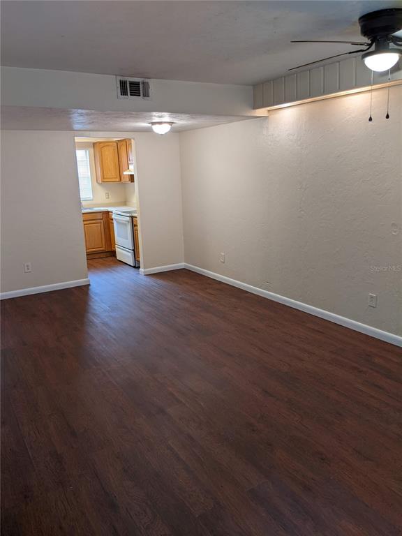 A living room with dark wood-look flooring leads into a kitchen with wooden cabinets — 4123 SW 15TH PLACE UNIT 3, GAINESVILLE, FL