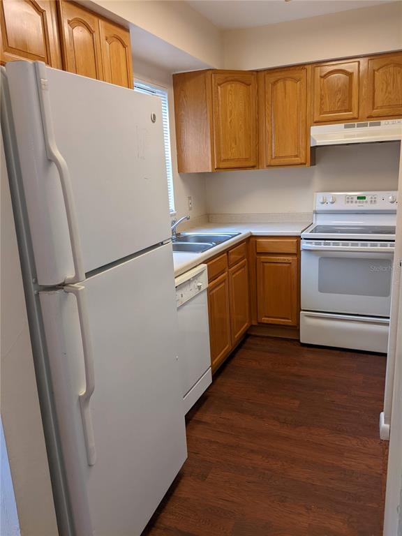 A kitchen features wood cabinets, white appliances, a double sink, and dark wood-look flooring — 4123 SW 15TH PLACE UNIT 3, GAINESVILLE, FL