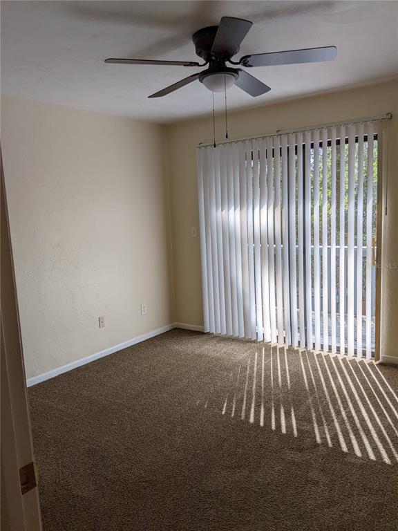 A bedroom with brown carpet, a ceiling fan, and vertical blinds covering a sliding door — 4123 SW 15TH PLACE UNIT 3, GAINESVILLE, FL