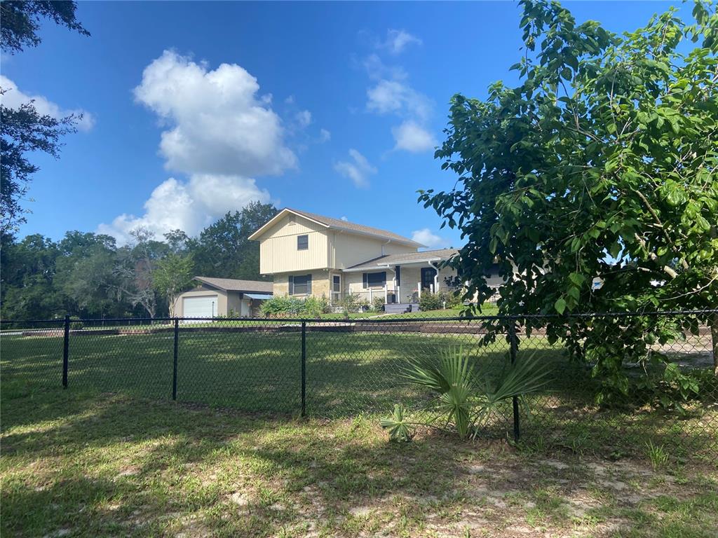 A two-story house with light siding and a detached garage sits behind a chain-link fence — 280 W VIRGINIA AVENUE, DELAND, FL