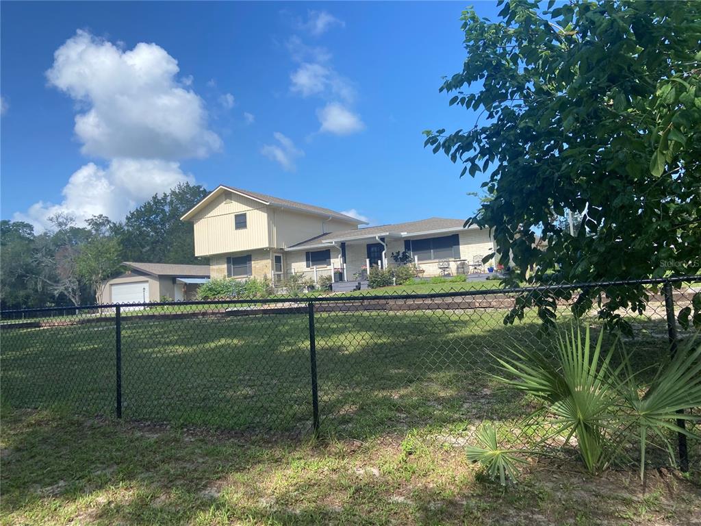 A two-story house with a light-colored exterior sits behind a chain-link fence — 280 W VIRGINIA AVENUE, DELAND, FL