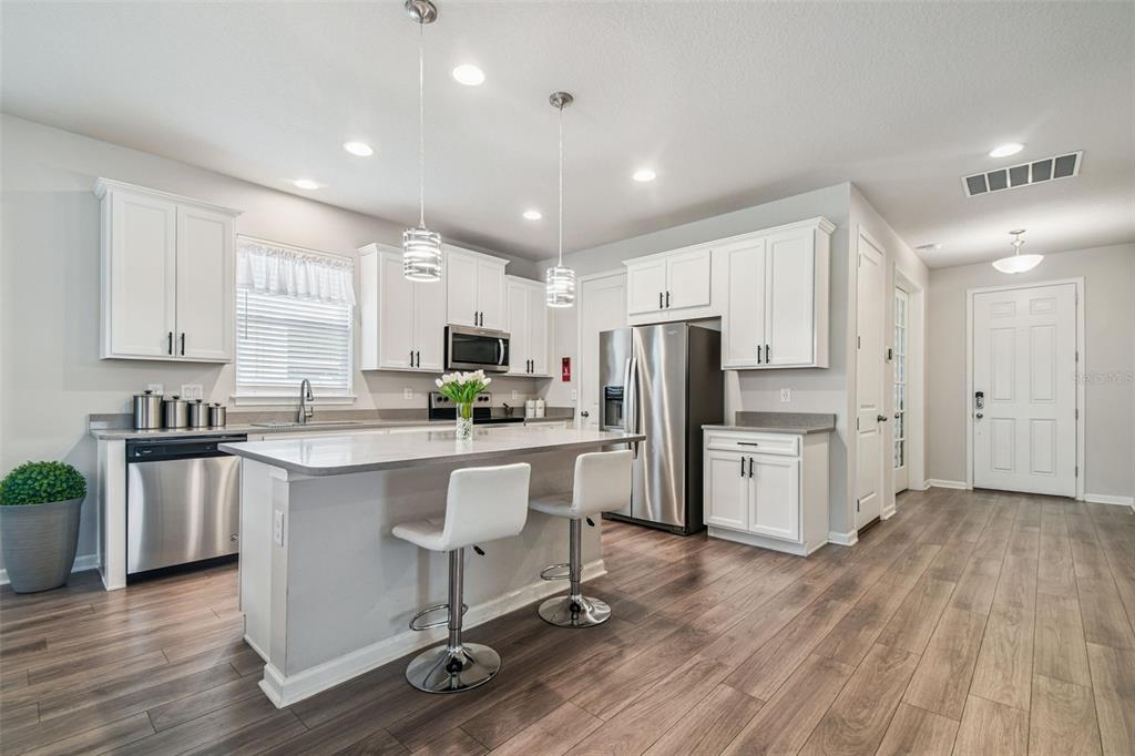 A modern kitchen features white cabinets, stainless steel appliances, a center island, and wood flooring — 11514 CEDAR VALLEY DRIVE, RIVERVIEW, FL
