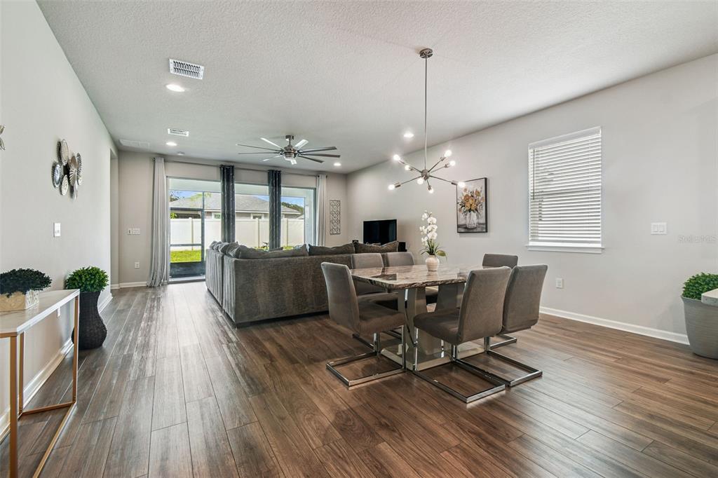 An open-concept living and dining area features wood-look flooring, a modern chandelier, and sliding doors — 11514 CEDAR VALLEY DRIVE, RIVERVIEW, FL