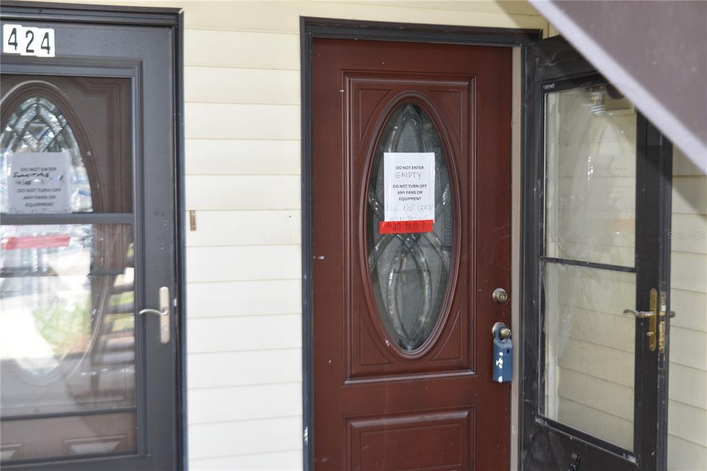 Two exterior doors with signs and a lockbox on a building with light siding — 420 MOORINGS COVE DRIVE UNIT 420, TARPON SPRINGS, FL