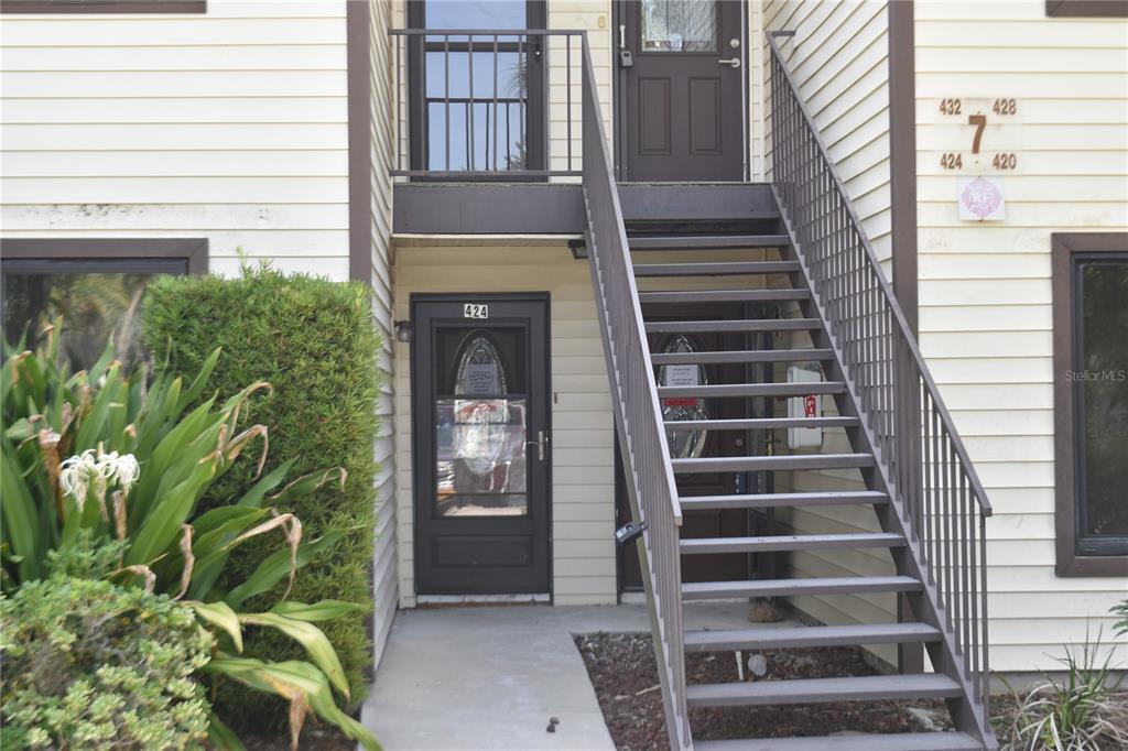 An exterior view of a two-story apartment building with a metal staircase and numbered doors — 420 MOORINGS COVE DRIVE UNIT 420, TARPON SPRINGS, FL