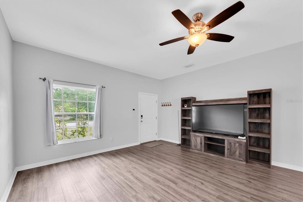 A living room features light gray walls, wood-look flooring, a ceiling fan, and a media console — 5876 78TH AVENUE N, PINELLAS PARK, FL