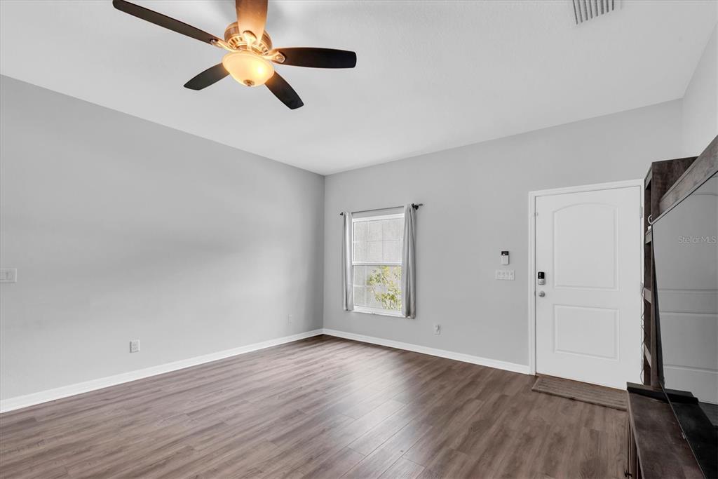 An empty room features light gray walls, wood-look flooring, a ceiling fan, and a white door — 5876 78TH AVENUE N, PINELLAS PARK, FL
