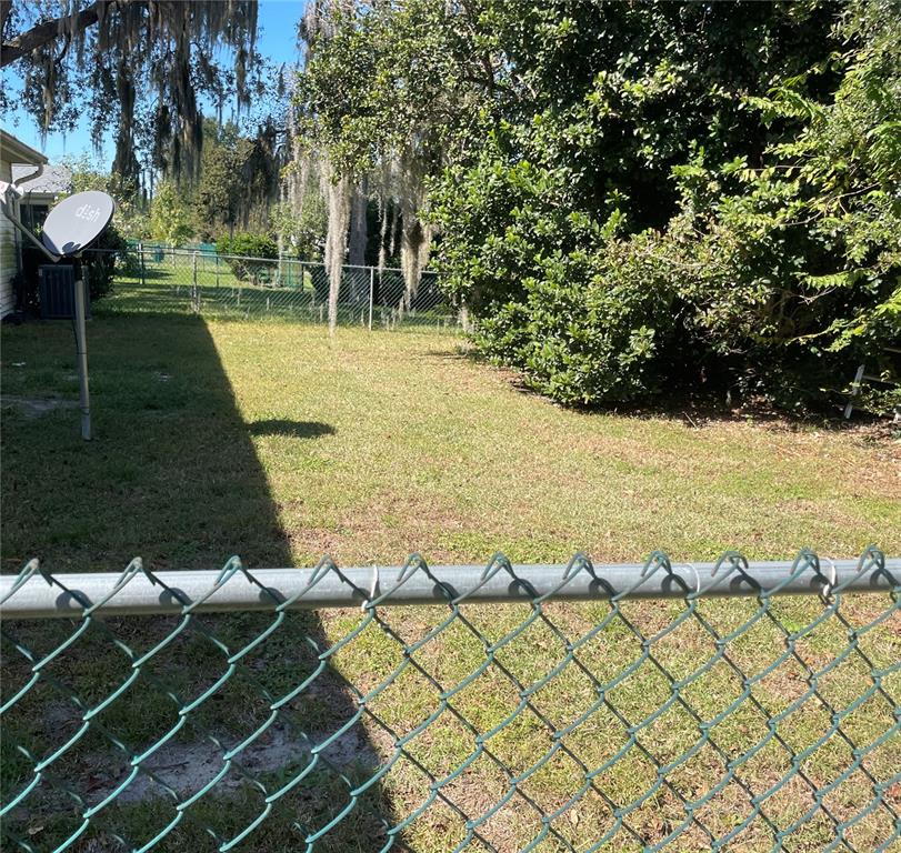 A grassy backyard features a chain-link fence, a satellite dish, and mature trees — 10967 SW 81ST AVENUE, OCALA, FL