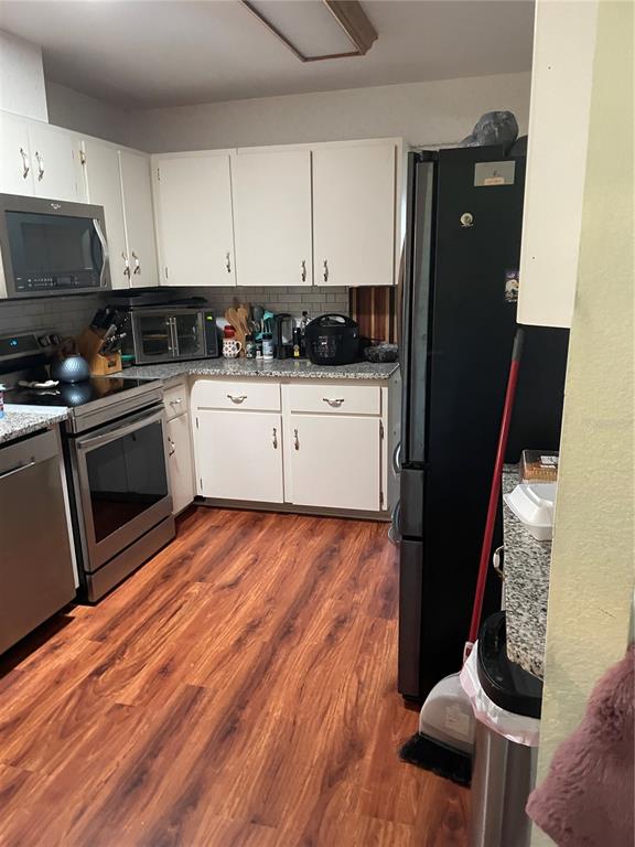 A kitchen features white cabinetry, stainless steel appliances, granite countertops, and wood-look flooring — 10967 SW 81ST AVENUE, OCALA, FL