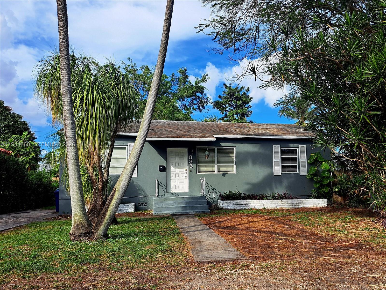 A gray single-story house features a white front door, a concrete walkway, and palm trees — 335 NW 102nd St, Miami FL 33150, MIAMI, FL