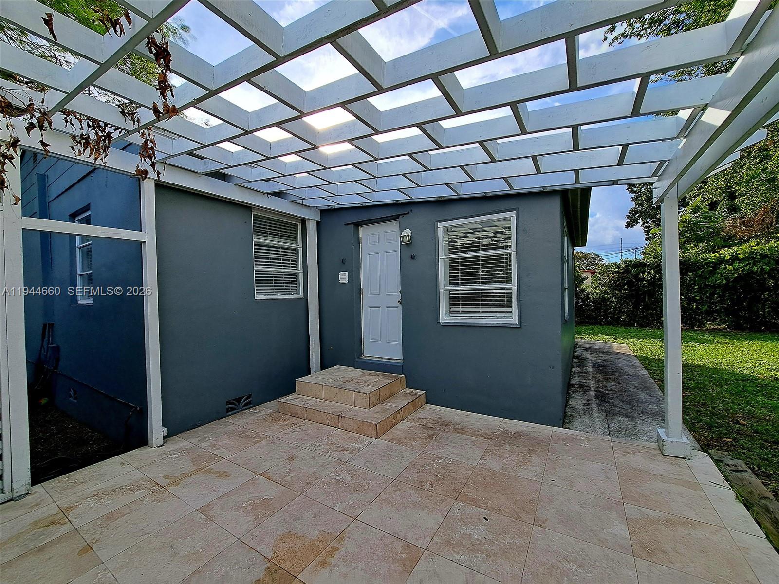 A gray exterior wall features a white door, tiled steps, and a white wooden pergola — 335 NW 102nd St, Miami FL 33150, MIAMI, FL
