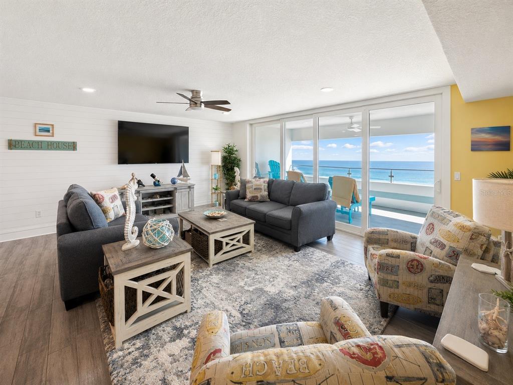A living room with gray sofas, patterned armchairs, and a balcony overlooking the ocean — 17400 GULF BOULEVARD N UNIT B-5, REDINGTON SHORES, FL