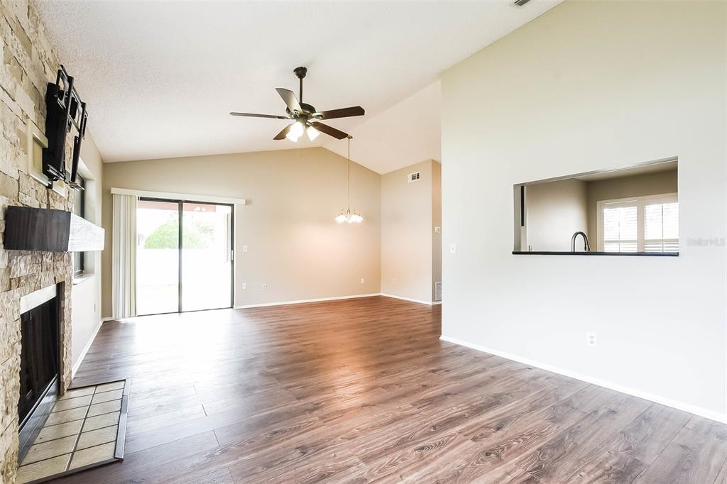 An open living area features wood-look flooring, a stone fireplace, and a vaulted ceiling — 7313 RADIANT CIRCLE, ORLANDO, FL