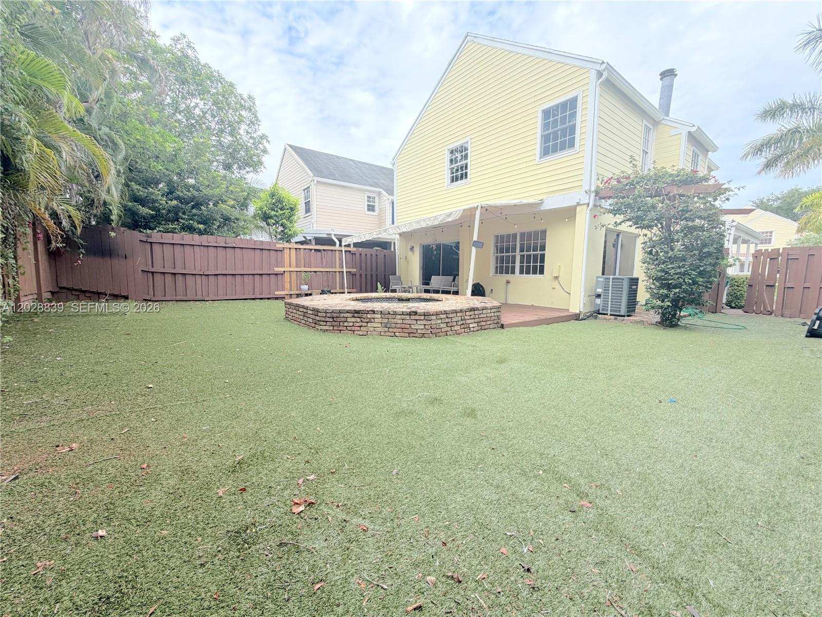 A yellow two-story house features a brick fire pit on a synthetic grass backyard — 11921 SW 117th Ct, Miami FL 33186, MIAMI, FL