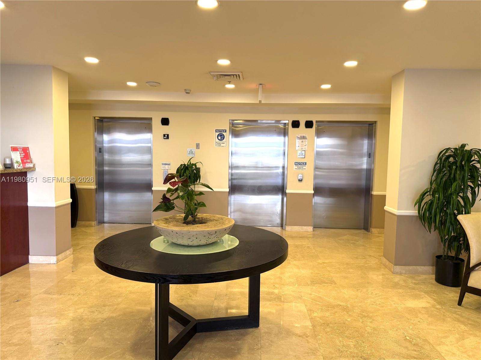 A lobby area features three stainless steel elevators, a round table with a plant, and tile floors — 900 SW 8th St # 604, Miami FL 33130, MIAMI, FL