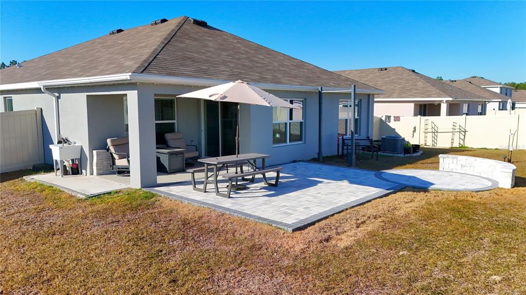 A backyard features a paved patio with a picnic table, umbrella, and a low stone wall — 7011 SW 136TH LANE, OCALA, FL