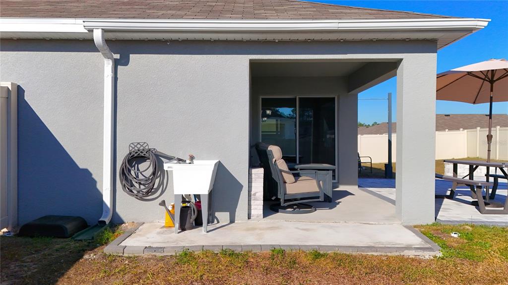 A gray stucco house exterior features a covered patio, a utility sink, and a downspout — 7011 SW 136TH LANE, OCALA, FL