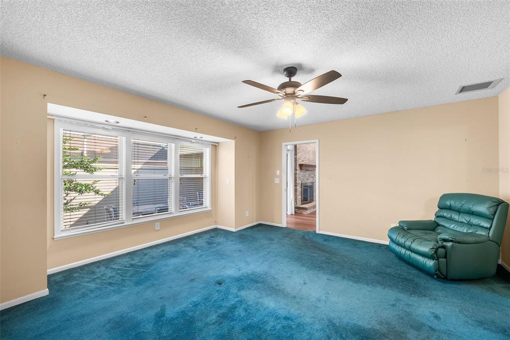 A room with teal carpeting, a ceiling fan, a large window, and a green recliner — 1767 SE 27TH LOOP, OCALA, FL