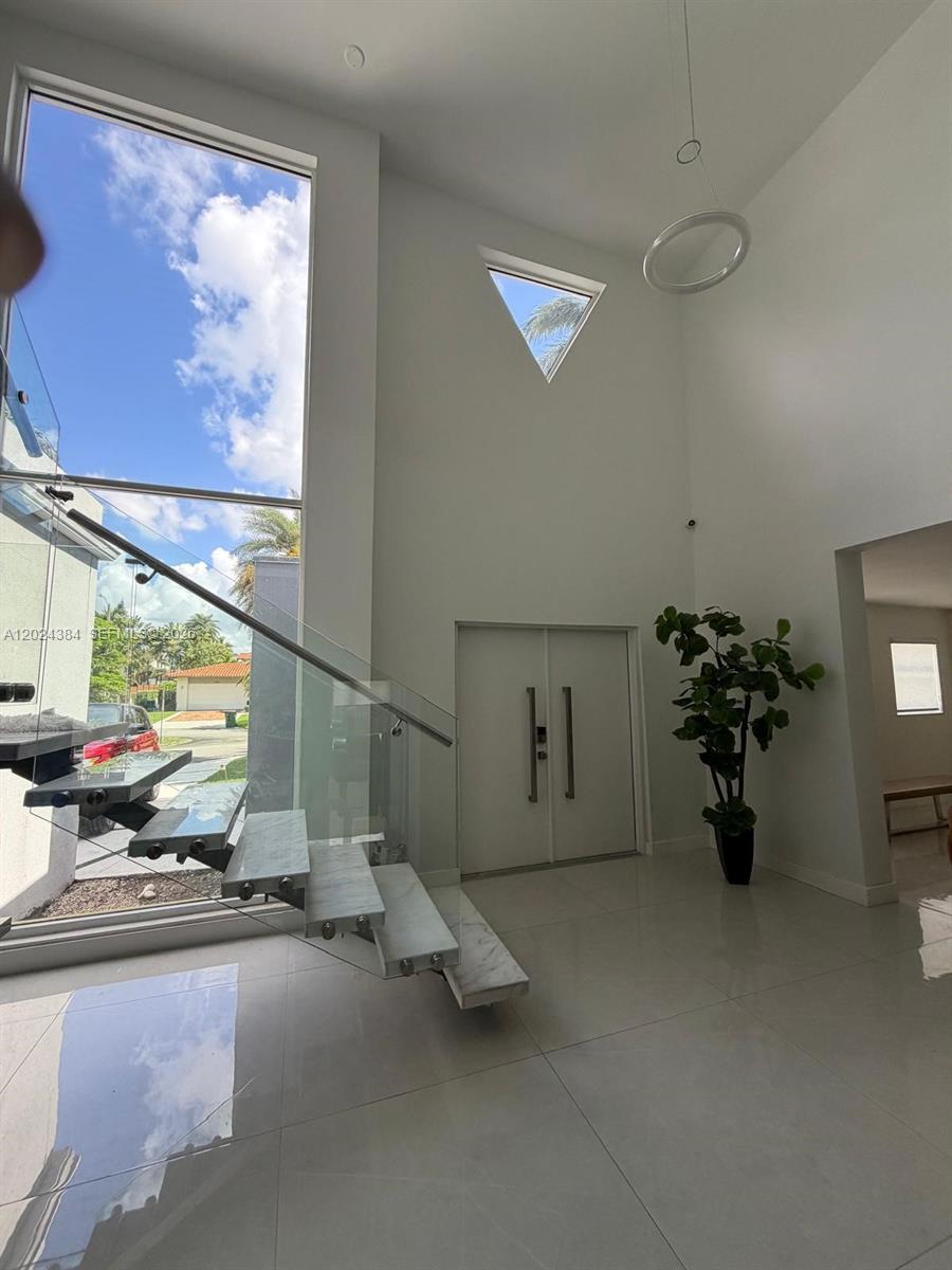 A modern entryway features a floating staircase, floor-to-ceiling windows, and white tile flooring — 10462 NW 130th St # 1, Hialeah Gardens FL 33018, HIALEAH GARDENS, FL