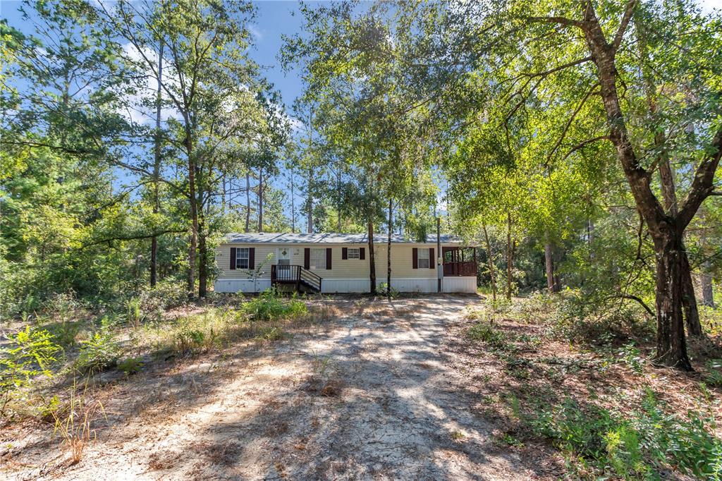 A single-story manufactured home sits in a wooded lot with a dirt driveway — 6639 NE 94TH AVENUE, BRONSON, FL