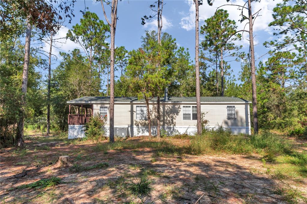 A single-story mobile home with light siding sits in a wooded lot with a porch — 6639 NE 94TH AVENUE, BRONSON, FL