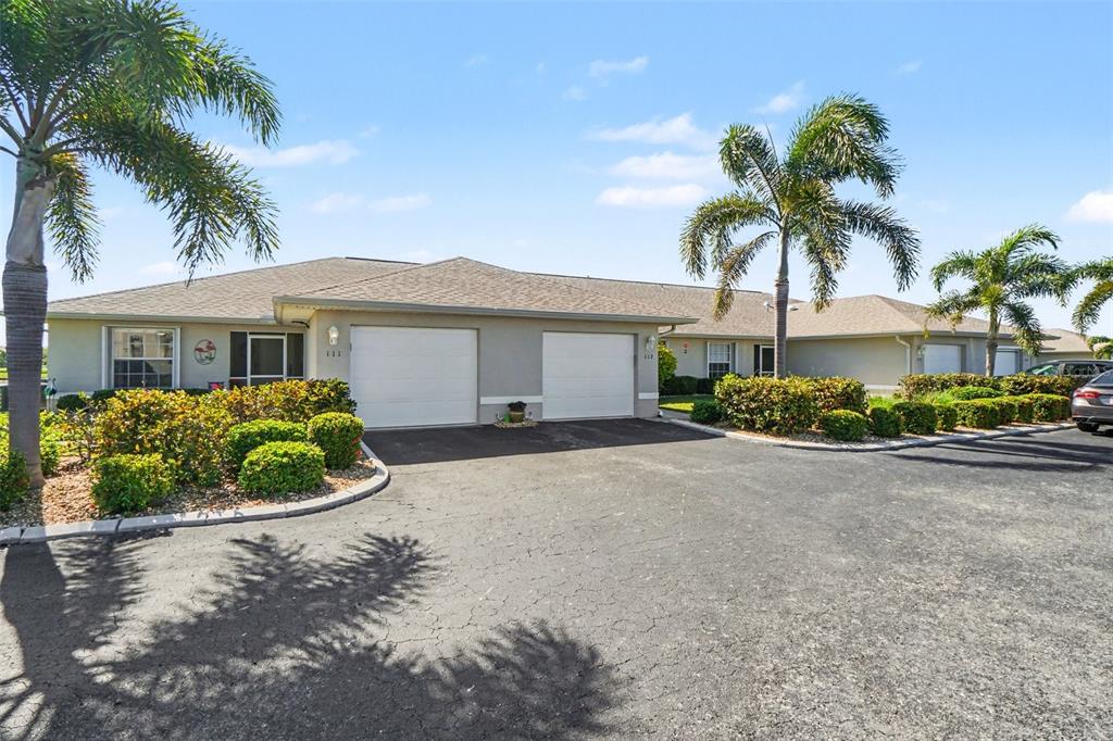A single-story duplex with two garage doors, palm trees, and a paved driveway — 26333 NADIR ROAD UNIT 111, PUNTA GORDA, FL