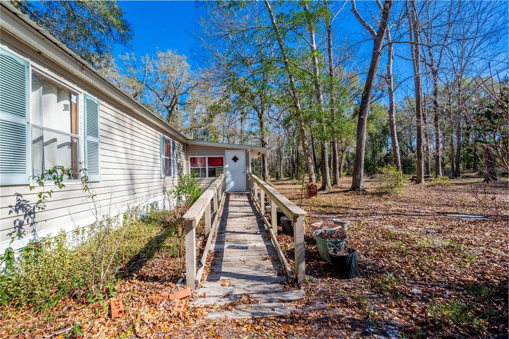 A wooden wheelchair ramp leads to the white front door of a beige mobile home — 383 NE 355TH AVENUE, OLD TOWN, FL