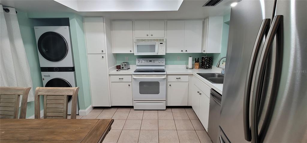 A kitchen features white cabinets, a stacked washer and dryer, and stainless steel appliances — 320 BARCELONA DRIVE UNIT 320, BRADENTON, FL