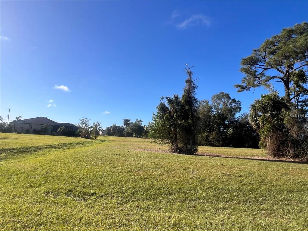 A grassy, open lot features scattered trees and a house in the distance — 16810 ACAPULCO ROAD, PUNTA GORDA, FL